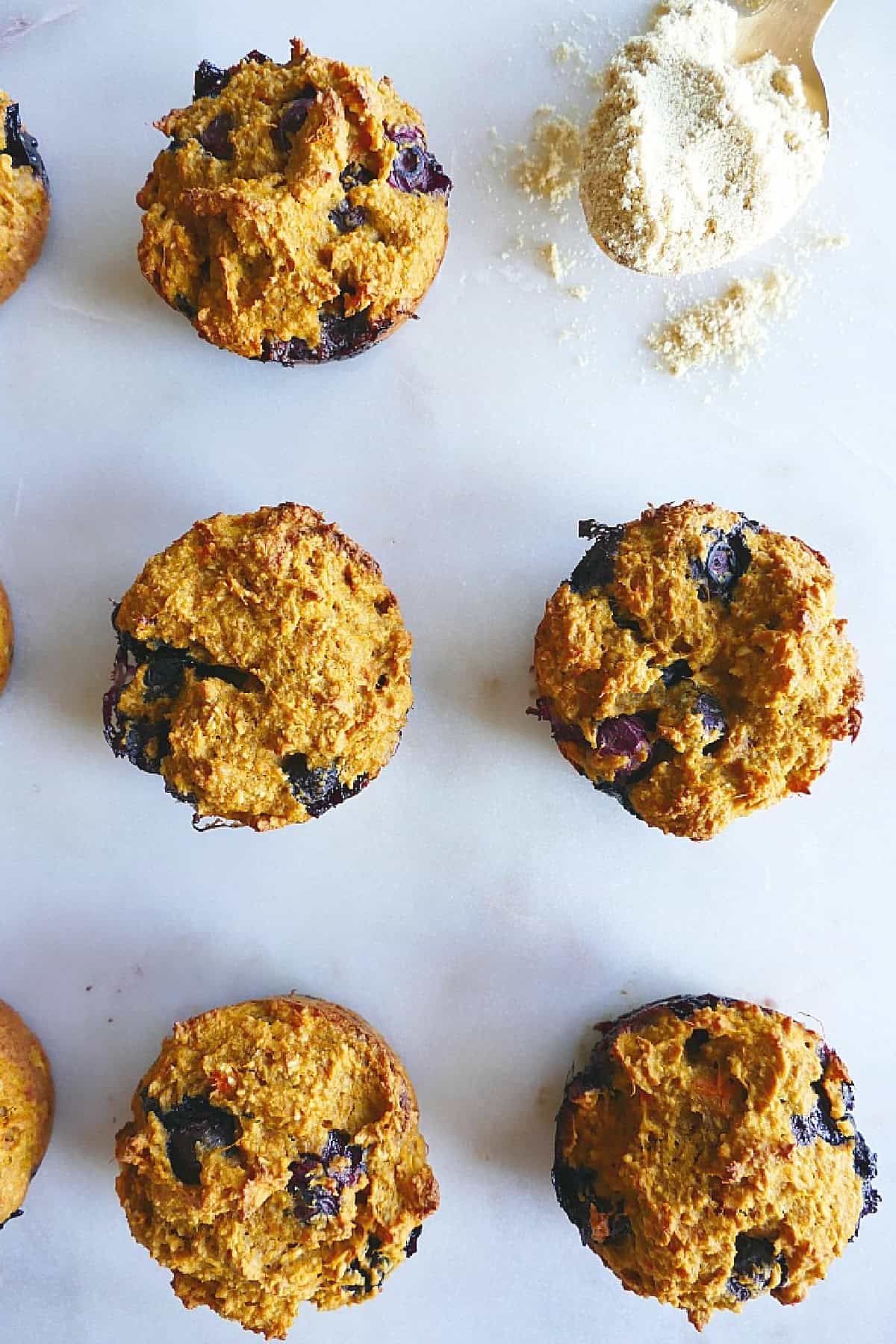 5 blueberry muffins on a counter next to a spoonful of milled flaxseed