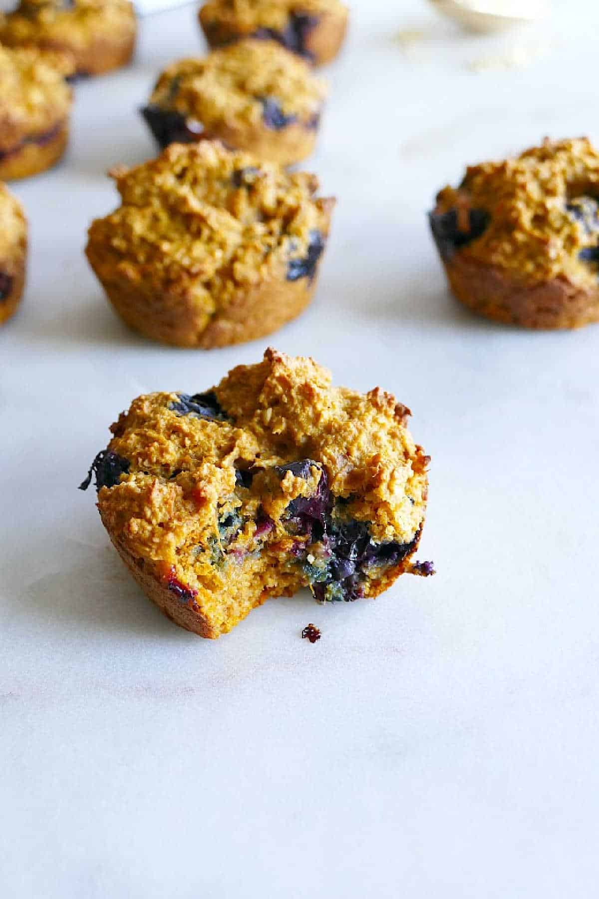 one blueberry muffin with a bite taken out of it in front of other muffins