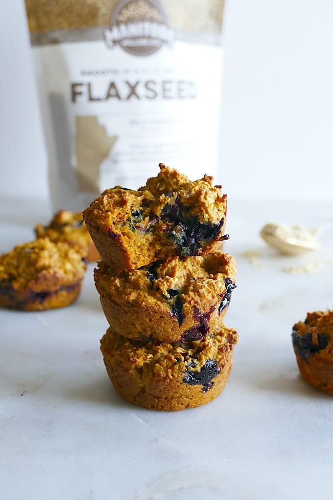 three blueberry flax muffins on top of each other with the flaxseed package in the back