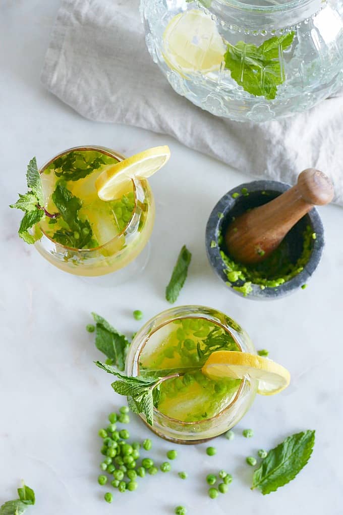 two kombucha mocktails garnished with lemon slices and mint leaves on a counter next to ingredients