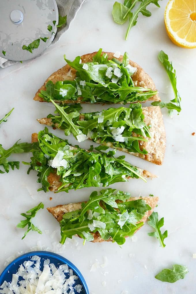 whole wheat pita with arugula on top sliced into 4 triangle pieces on a counter