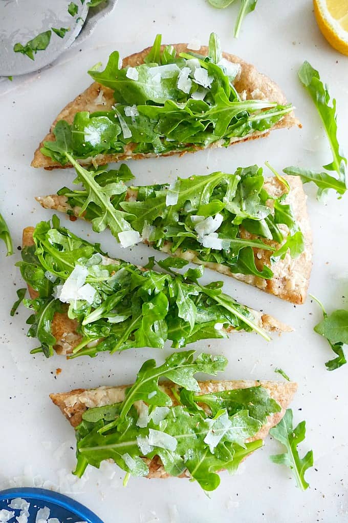 overhead shot of a pita pizza with arugula on top sliced into 4 pieces