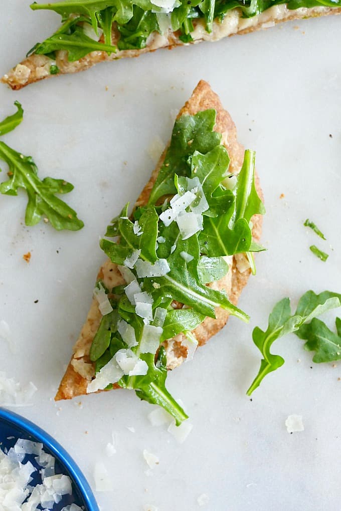 one slice of pita pizza with arugula and grated parmesan on top on a counter