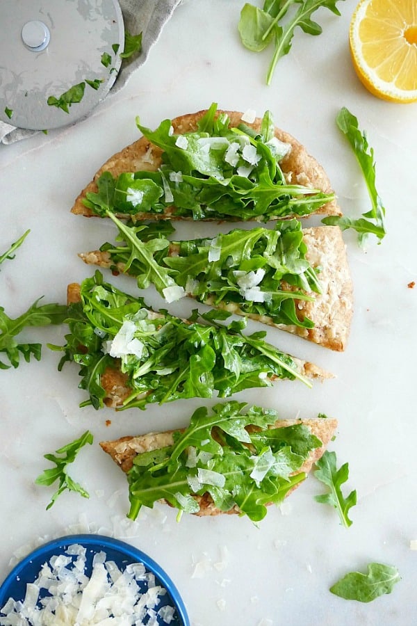 pita pizza topped with arugula sliced into four slices on a marble counter