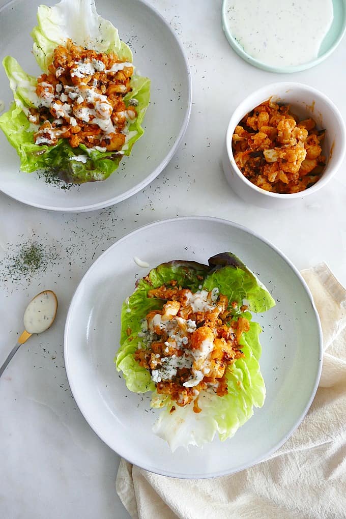 two plates with butter lettuce and buffalo cauliflower on a white countertop