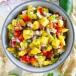 fresh mango salsa in a serving bowl surrounded by ingredients on a counter