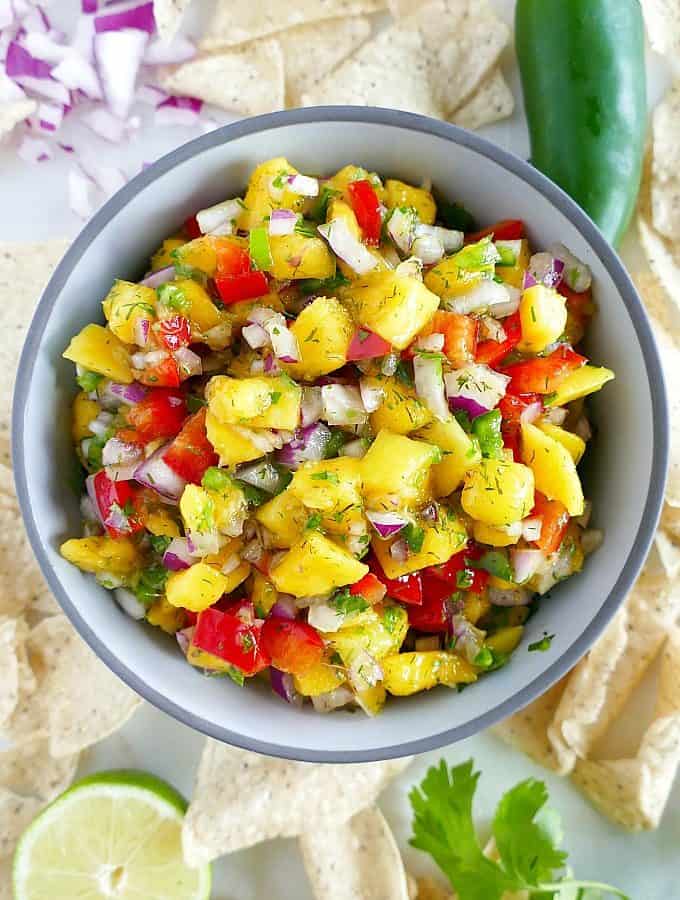 fresh mango salsa in a serving bowl surrounded by ingredients on a counter