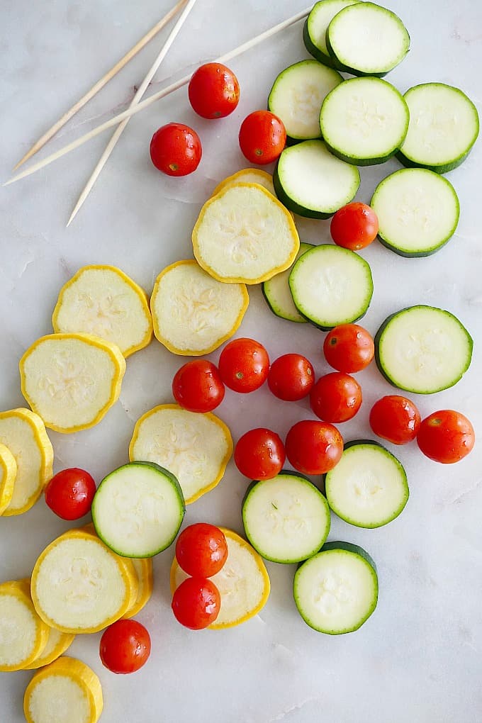 sliced yellow squash and zucchini with cherry tomatoes and skewers on a counter