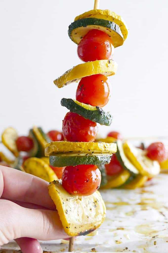side view of a veggie skewer with a hand holding it upright