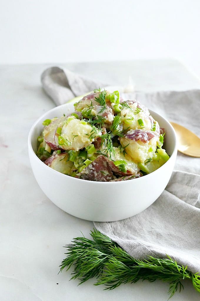 white bowl filled with potato salad on a gray napkin with a white background