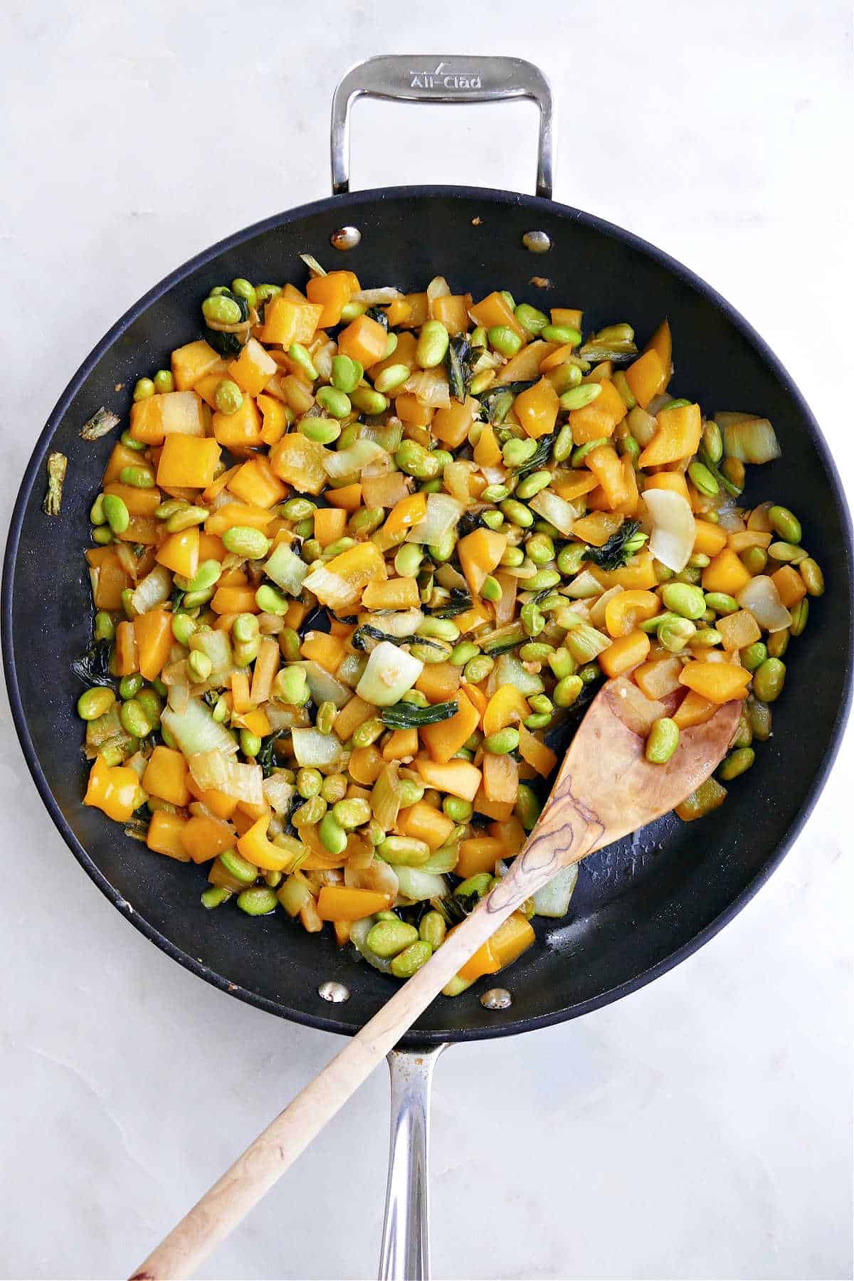 Bok Choy Mango Stir Fry cooking in a large black skillet with a wooden spoon