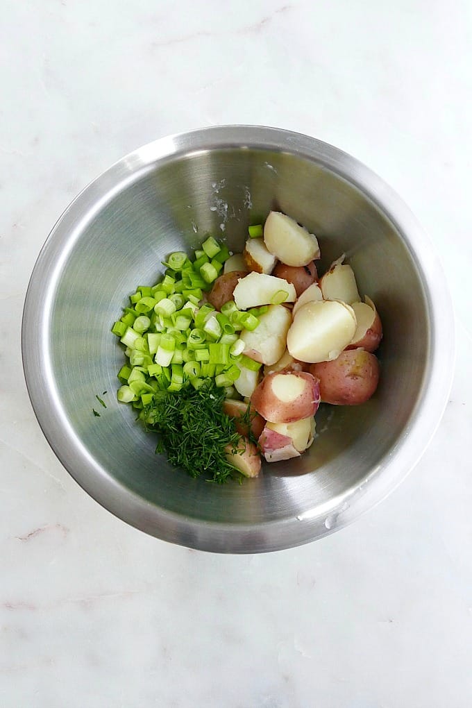 silver mixing bowl with scallions, potatoes, and fresh dill on a counter