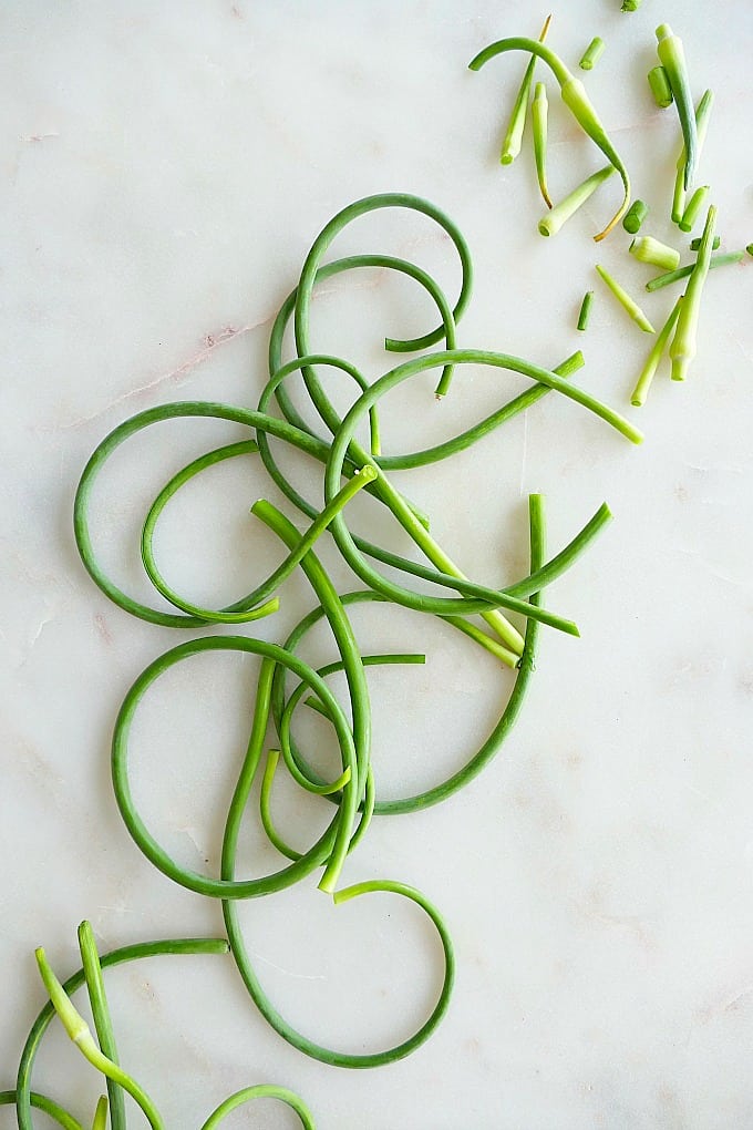 trimmed garlic scapes spread out on a white counter next to each other