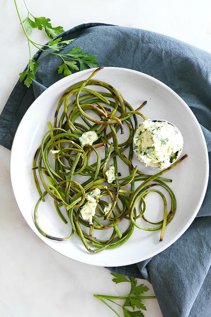 charred garlic scapes on a plate with a bowl of parsley butter