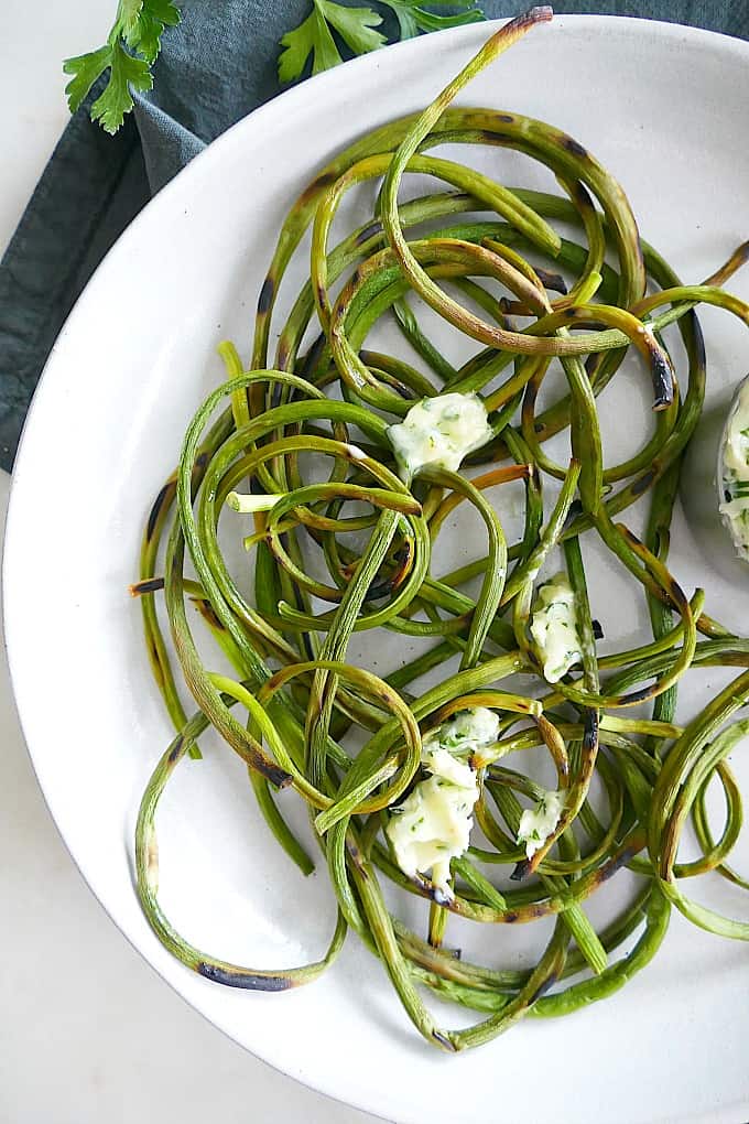 charred garlic scapes with dollops of parsley butter on a plate