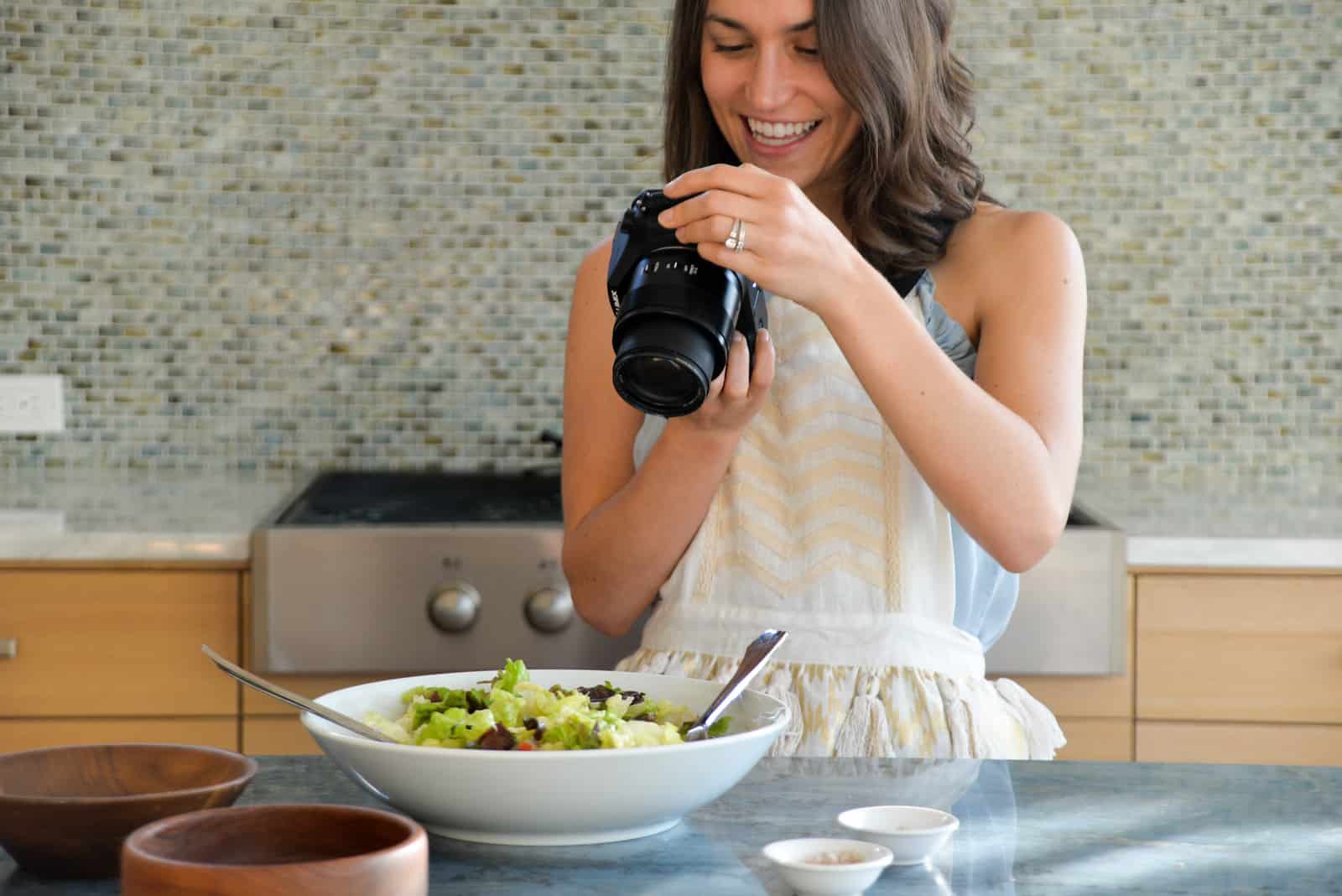 image of woman holding a camera and taking a photo of a bowl of salad in a kitchen