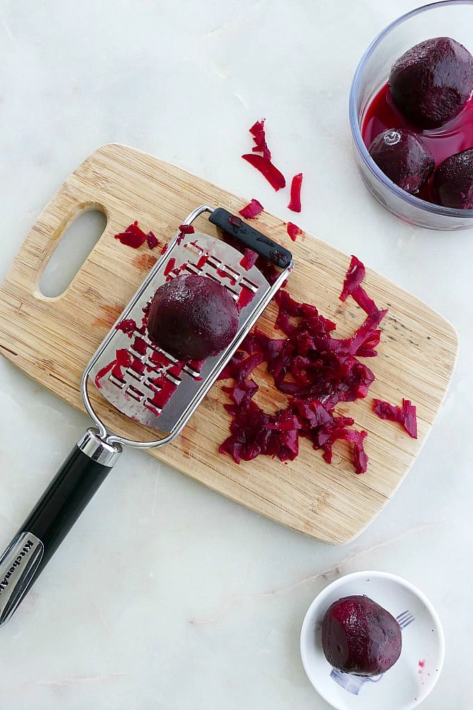 beets on top of a hand grater on a bamboo cutting board