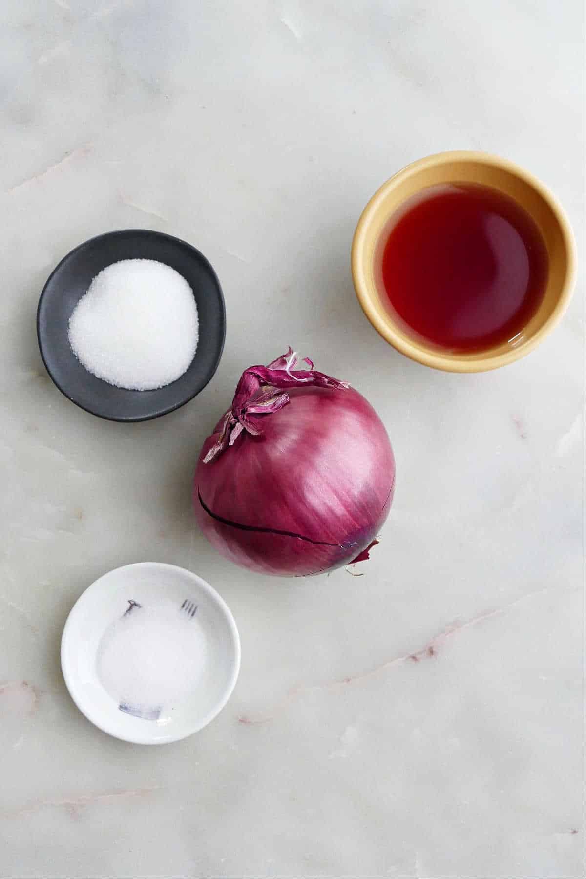 sugar, red wine vinegar, salt, and a red onion next to each other on a counter