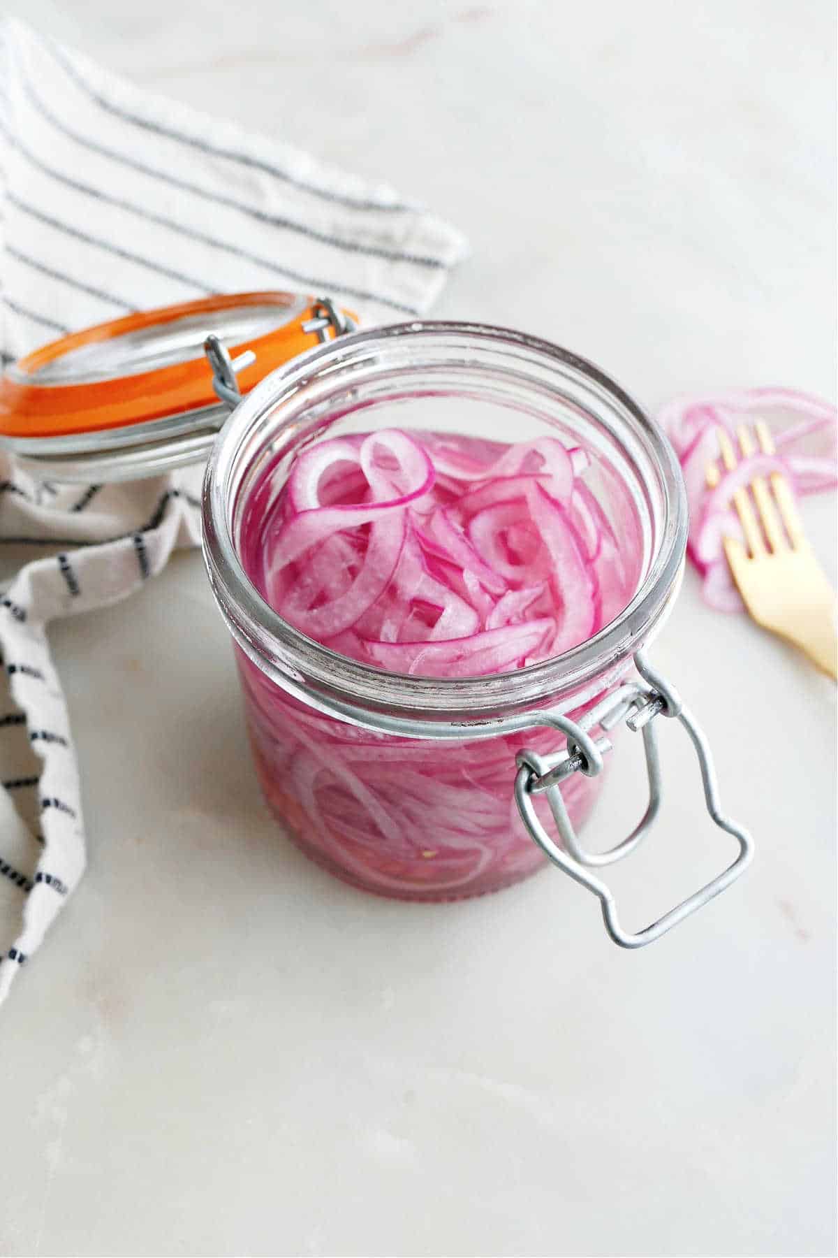 pickled red onions sitting in a brine in a jar on a counter