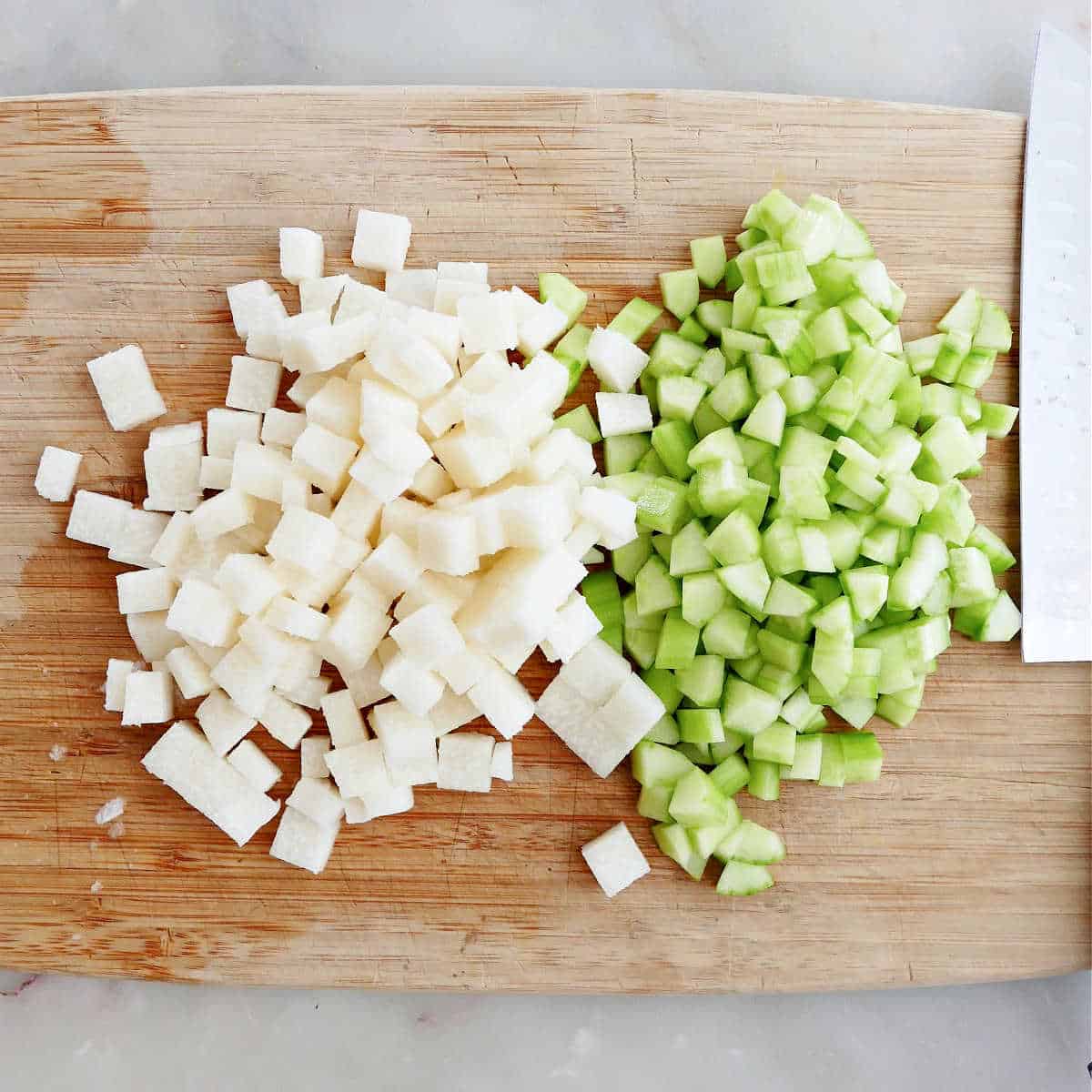 diced jicama and cucumber on a cutting board next to a chef's knife