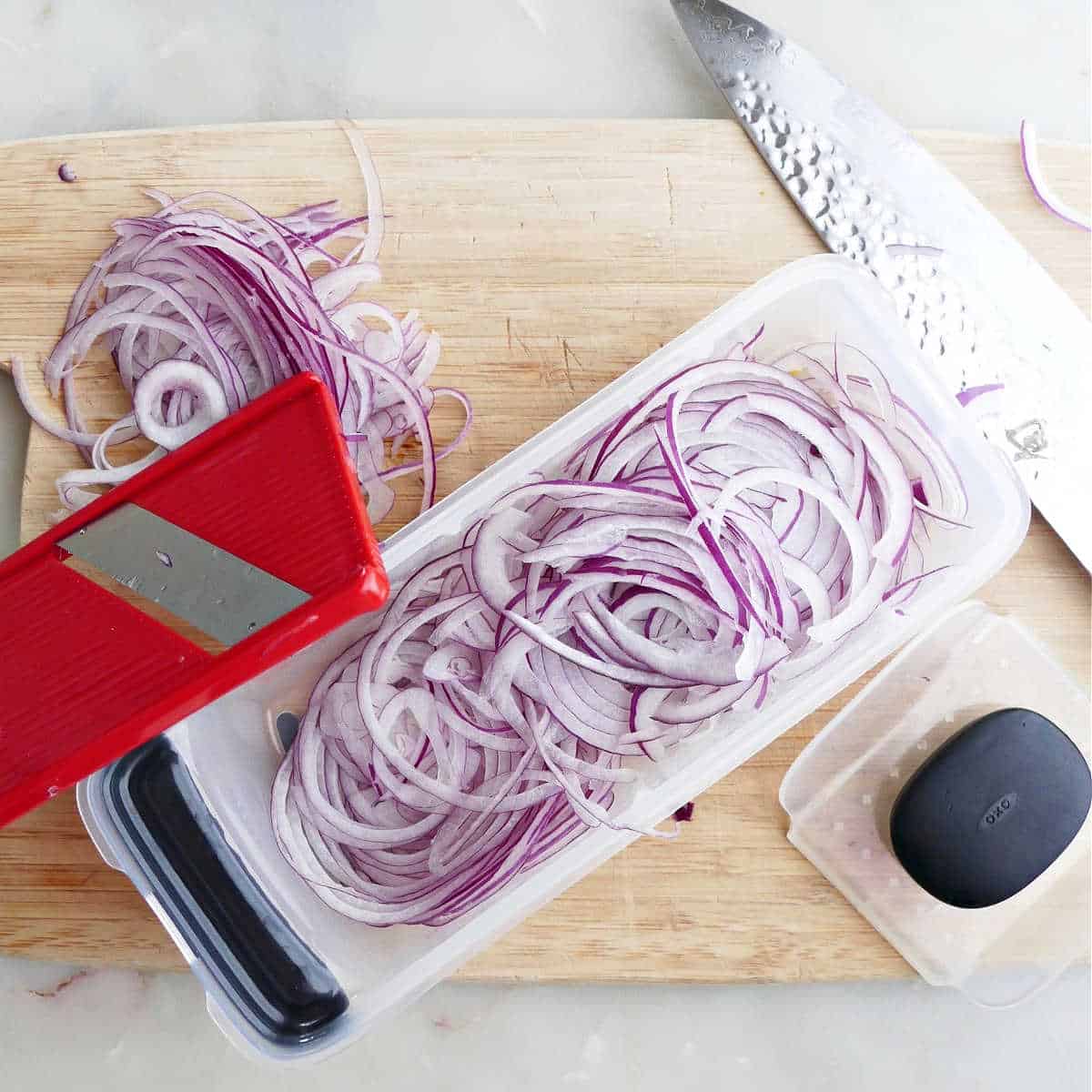 thinly sliced red onion in a mandolin on top of a cutting board