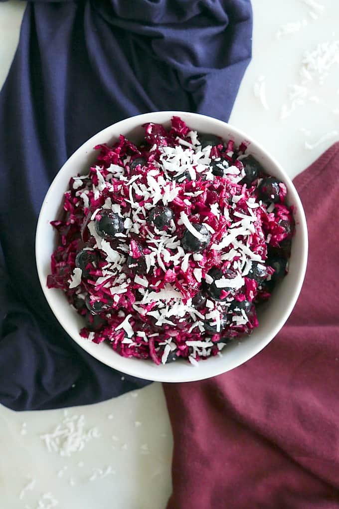 shredded beet slaw in a white bowl topped with blueberries and coconut on a counter