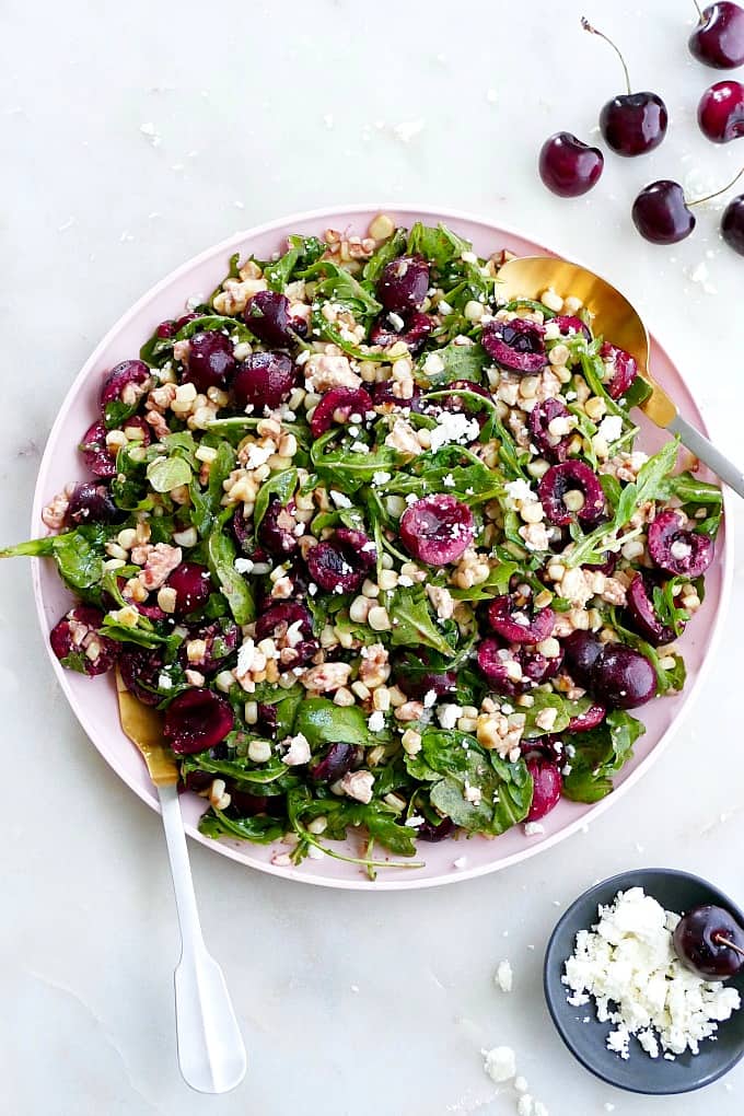 Sweet corn and cherry arugula salad on a pink serving tray with utensils