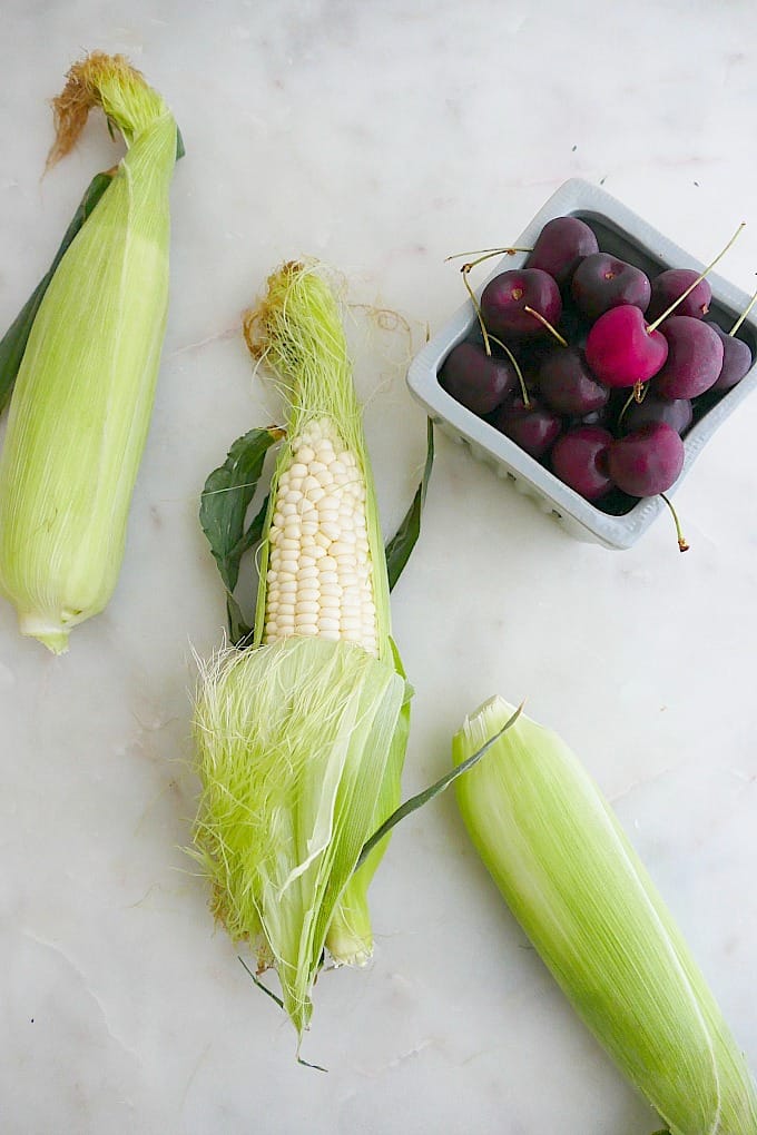 corn husks and cherries spread out next to each other on top of a counter