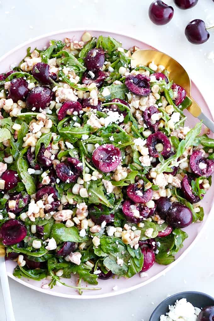 sweet corn and cherry arugula salad on a serving platter with gold utensils