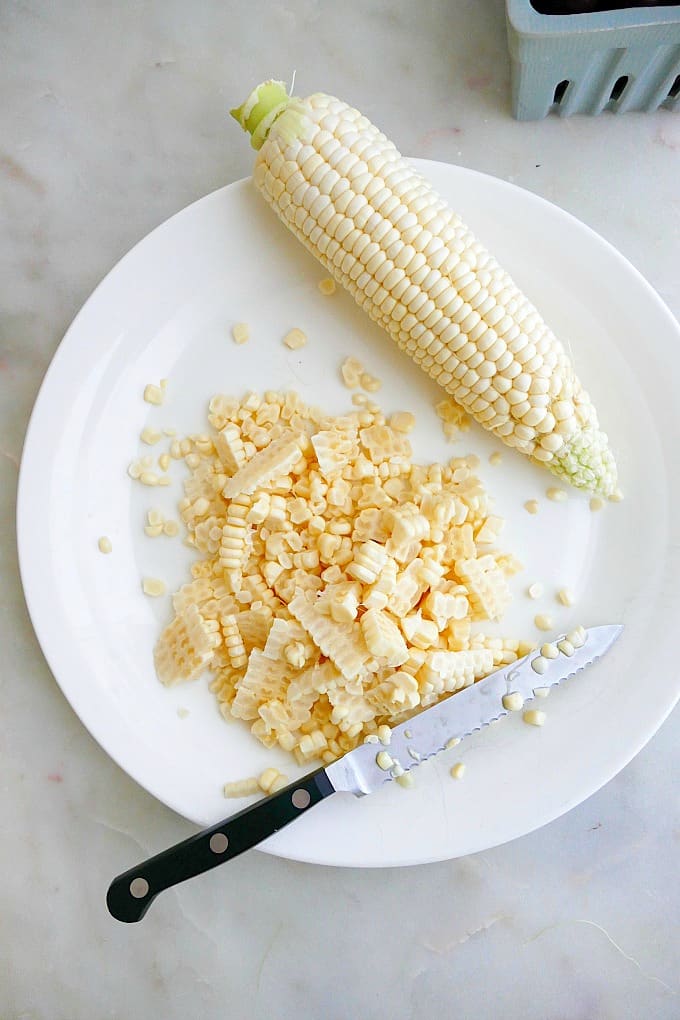 corn kernels next to a cob and a serrated knife on a white plate