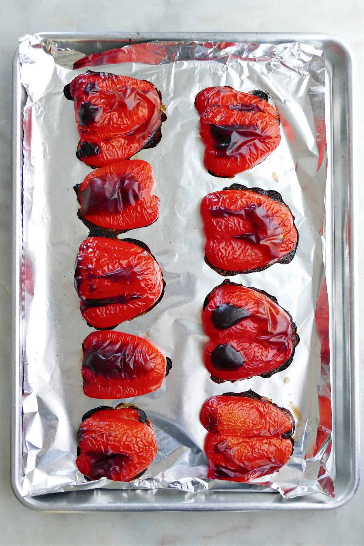nine slices of blackened red bell peppers on a baking sheet lined with foil