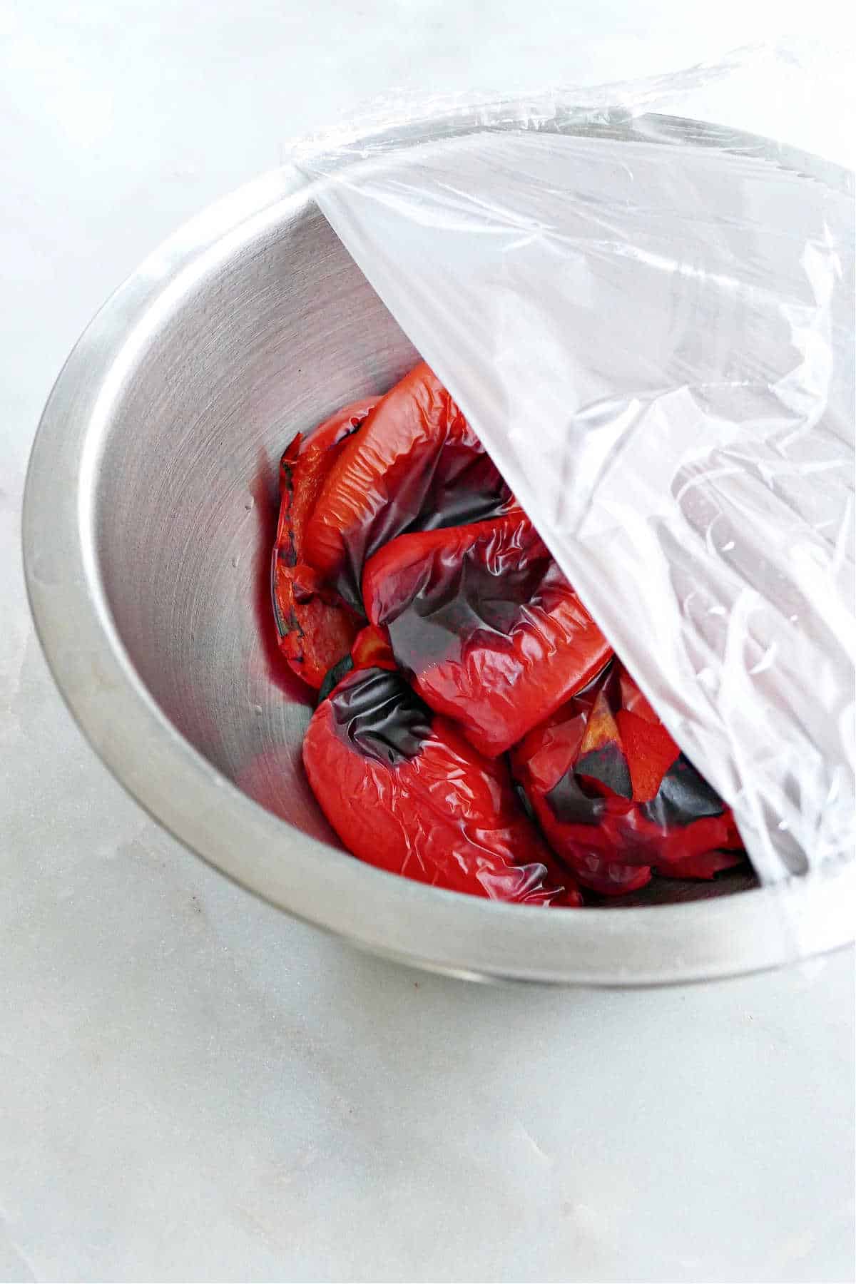 roasted red peppers in a large bowl halfway covered with plastic wrap