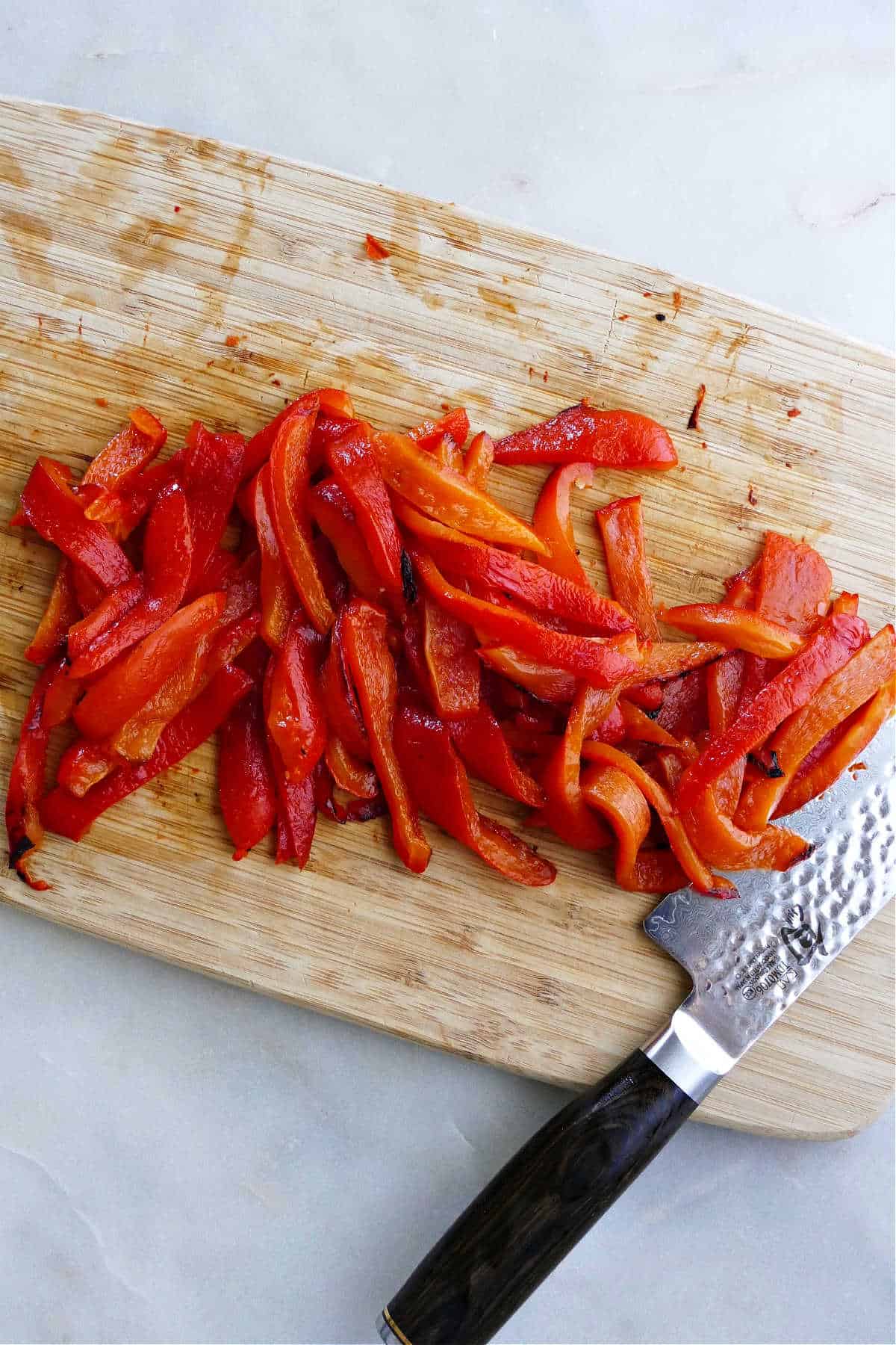roasted red peppers cut into thin strips on a cutting board with a knife