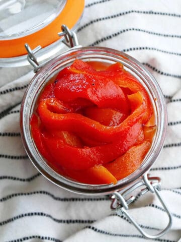 Italian roasted red peppers in a glass jar on top of a striped napkin