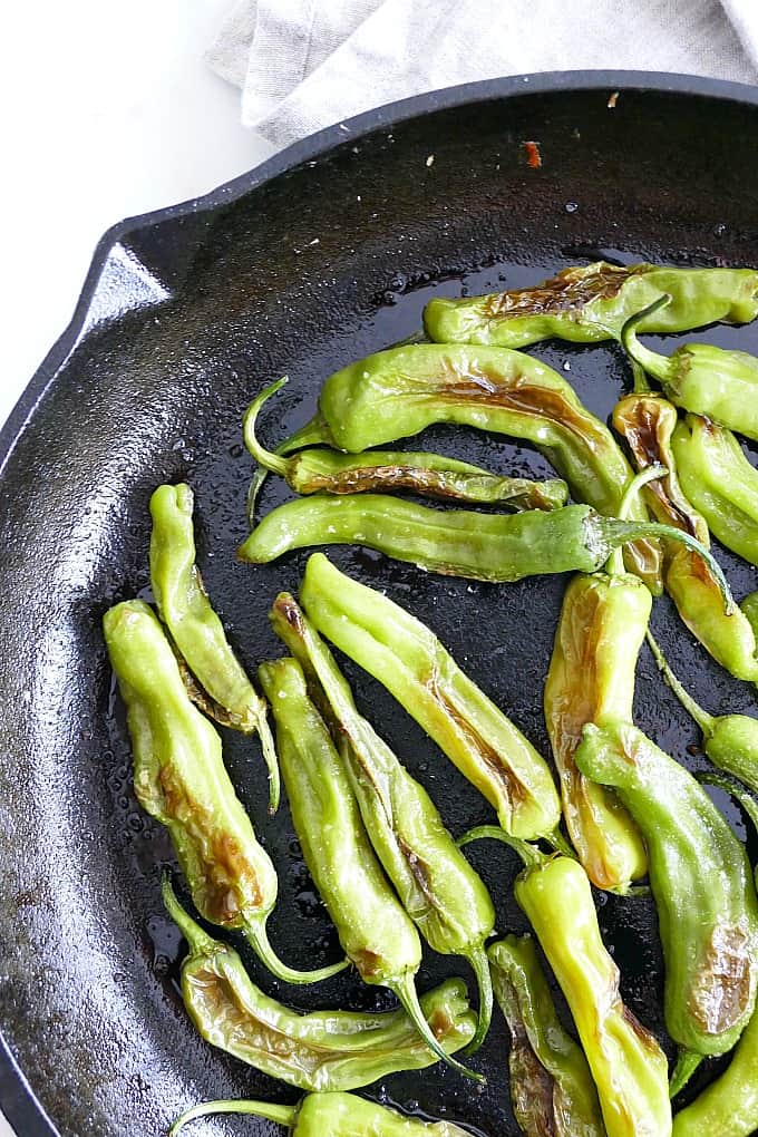 close up photo of Blistered Shishito Peppers sprinkled with salt in a cast iron skillet