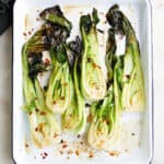 six roasted baby bok choy halves on a white rectangular tray on a counter