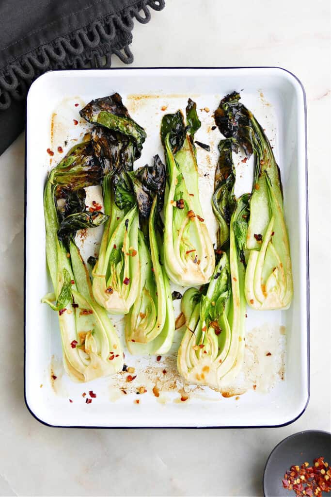 six roasted baby bok choy halves on a white rectangular tray on a counter