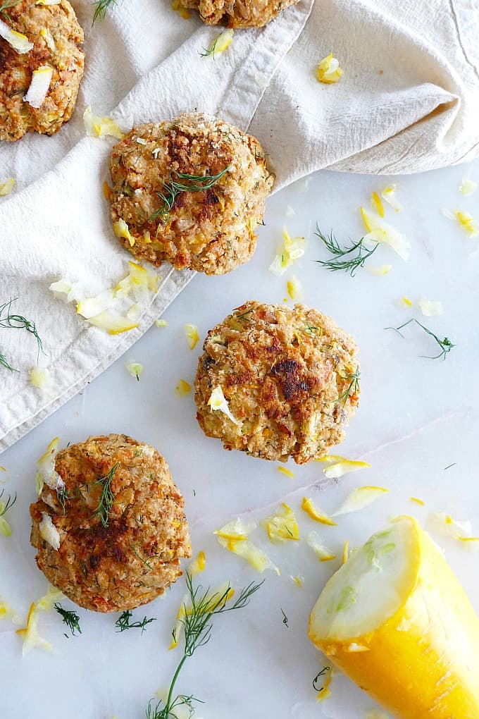 three dill salmon burgers on a counter with grated squash around them
