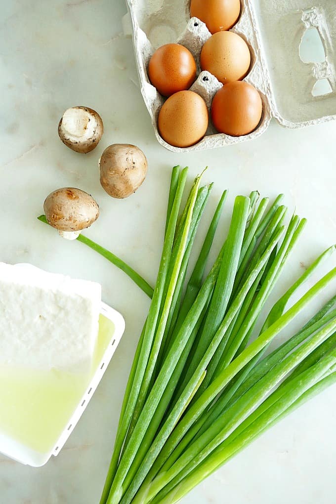 eggs, mushrooms, scallions, and feta cheese spread out on a counter next to each other