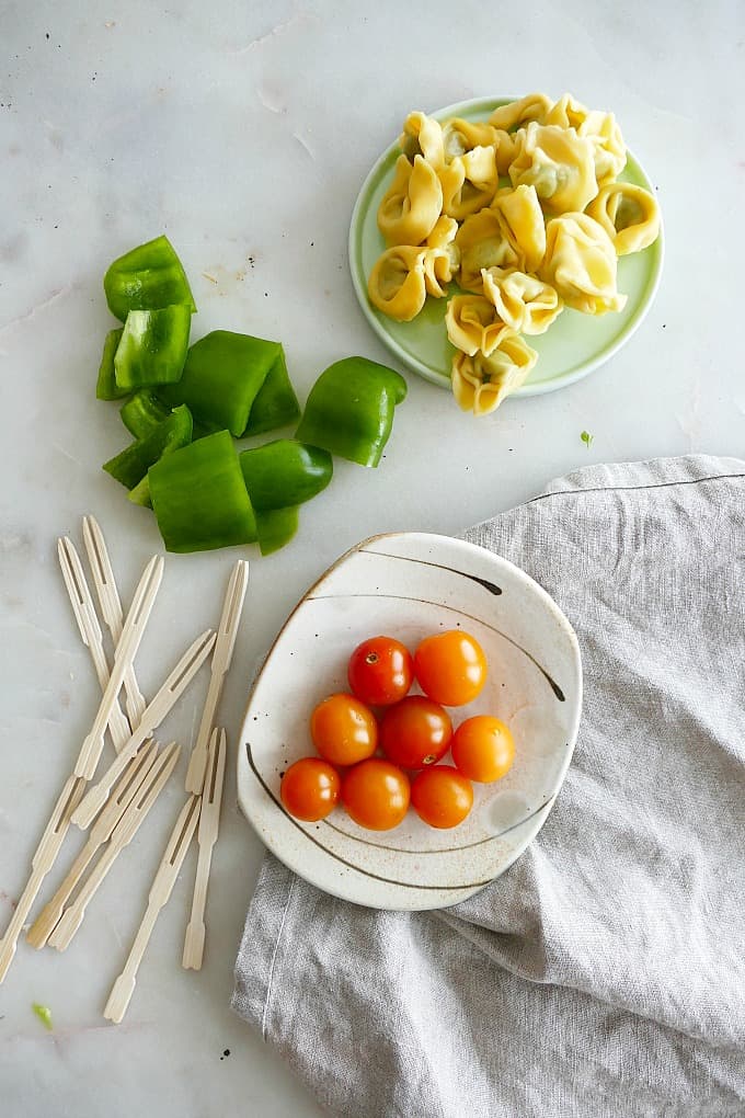 cooked tortellini, chopped bell pepper, cherry tomatoes, and toothpicks on a counter