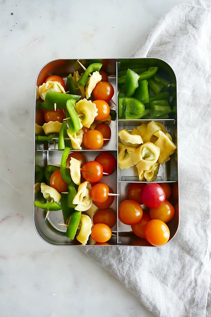 metal lunchbox filled with compartments of peppers, tomatoes, tortellini and finished skewers