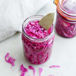 Pickled red cabbage in glass jars with seasonings on a counter.