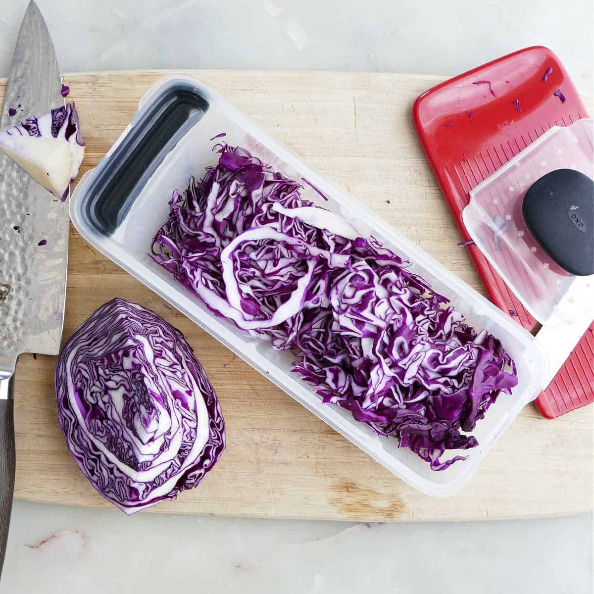 Red cabbage that was shredded with a mandoline on a cutting board.