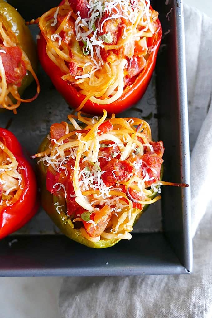 two Spaghetti Stuffed Bell Peppers in a baking dish on top of a napkin