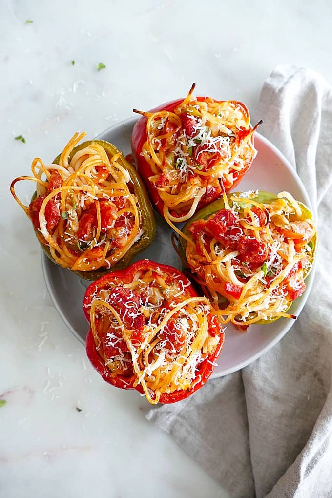 4 Spaghetti Stuffed Bell Peppers topped with grated cheese on a serving plate on counter