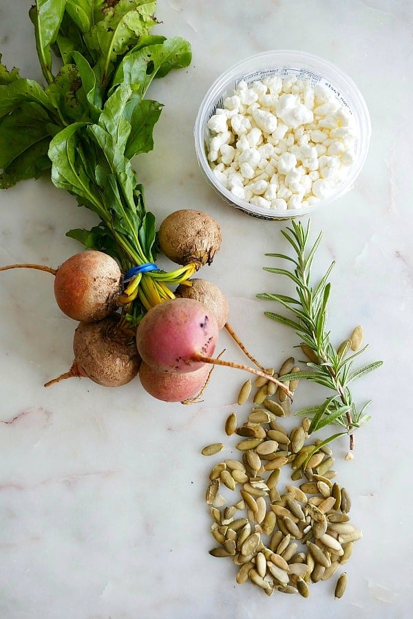 a bunch of golden beets, goat cheese crumbles, rosemary, pumpkin seeds on a counter