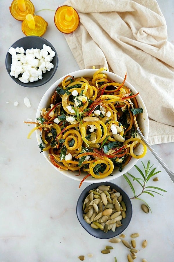 Spiralized Golden Beet Salad next to small bowls of goat cheese and pumpkin seeds