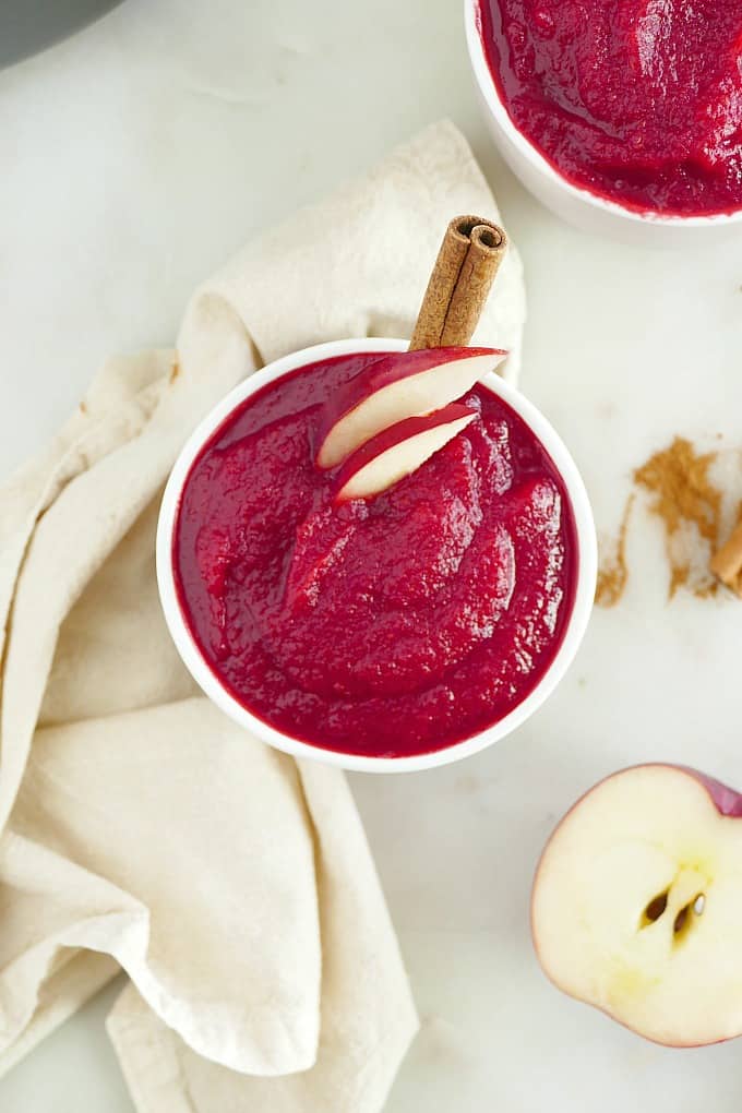 bright pink veggie applesauce in a bowl topped with apple slices and cinnamon stick