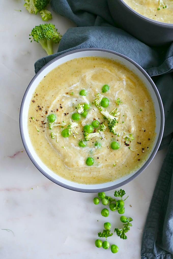 bowl of broccoli soup with potatoes and peas on a white counter next to blue napkin