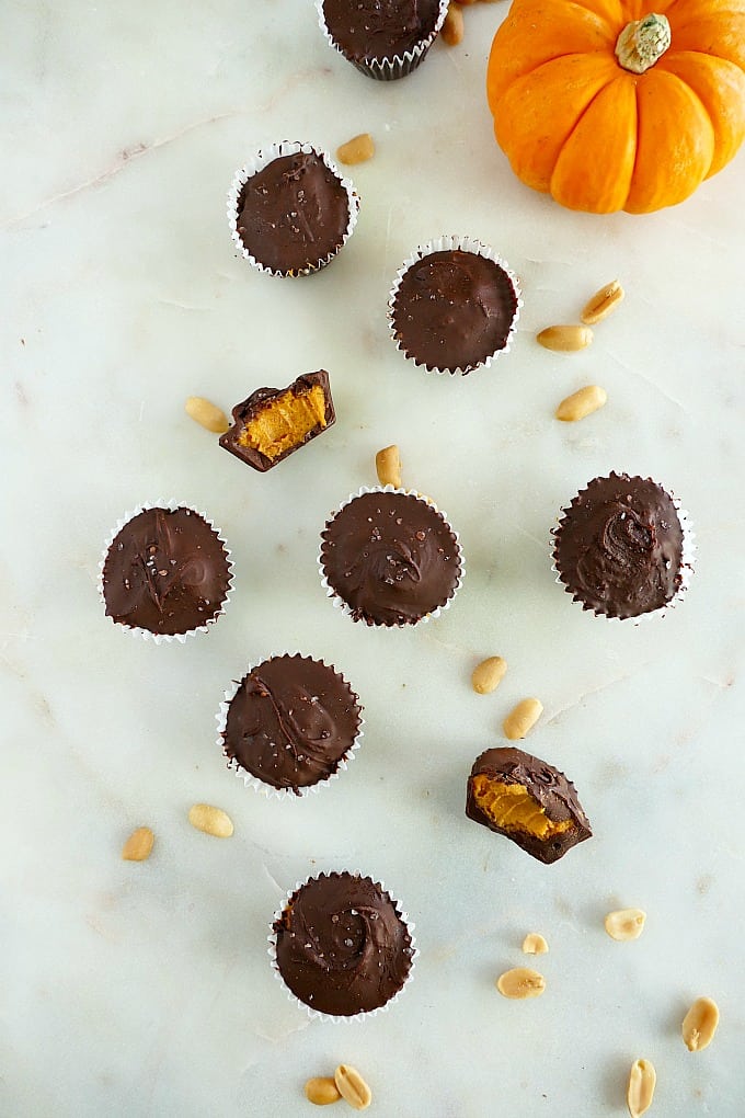 vegan peanut butter cups with pumpkin on a white countertop with peanuts and a mini pumpkin